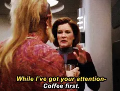 Captain Kathryn Janeway of the Federation Starship Voyager interrupts a crewmate with a terse, 'coffee first,' before taking a sip of coffee.